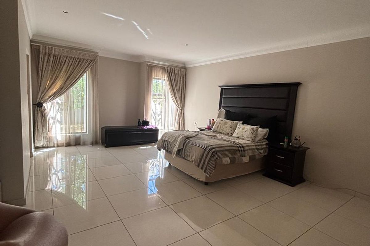 Spacious bedroom featuring large-format porcelain floor tiles, recessed downlighting, and dual sliding glass doors providing ample natural light.