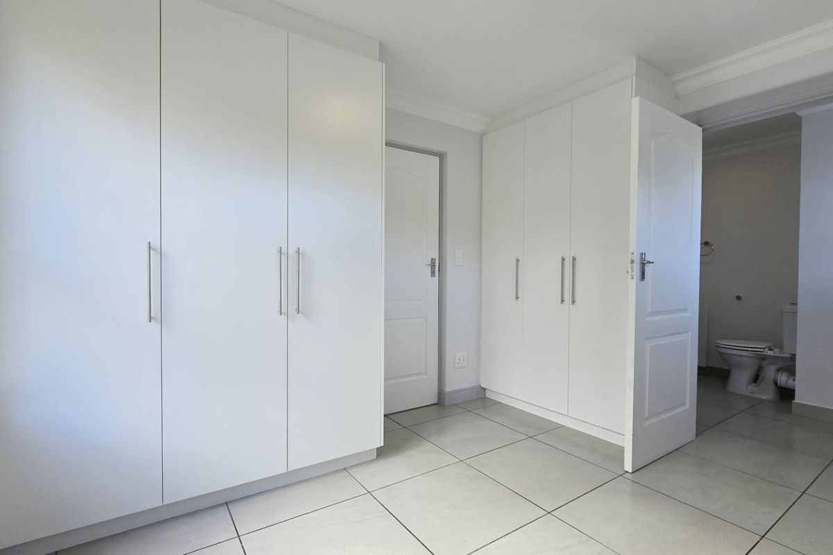 A bright bedroom featuring extensive built-in white cabinetry, tiled flooring, and direct access to an en-suite bathroom.
