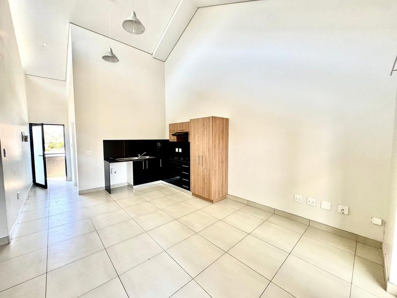 Spacious open-plan living area featuring high vaulted ceilings, tiled flooring, and a modern kitchen with built-in cabinetry and integrated appliances.