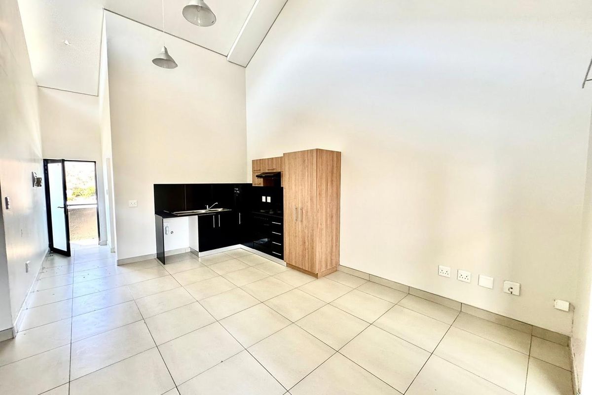 Spacious open-plan living area featuring high vaulted ceilings, tiled flooring, and a modern kitchen with built-in cabinetry and integrated appliances.