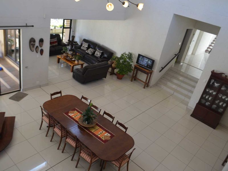 Spacious open-plan living and dining area featuring large format floor tiles, a central staircase, and sliding glass doors leading to an outdoor patio.
