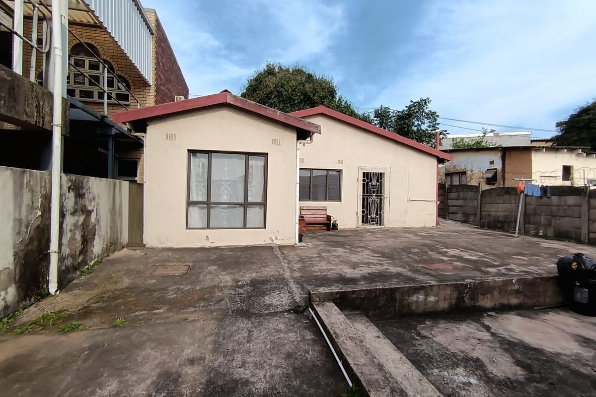 Rear view of the property featuring a large concrete patio area, security gate, and weathered exterior finishes.