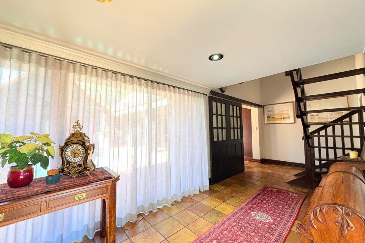 A bright living area featuring terracotta tile flooring, a timber staircase, and a sliding barn door, with large windows dressed in sheer curtains.