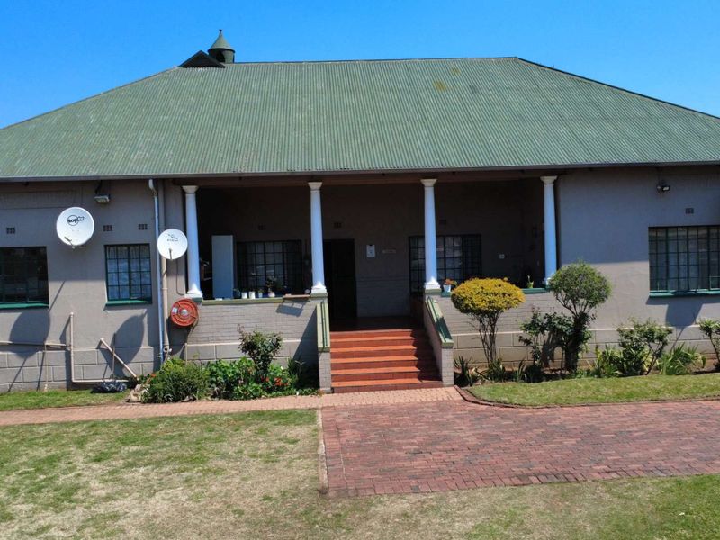 Front elevation of a single-story house featuring a covered veranda, brick steps, and a corrugated metal roof with a paved driveway.