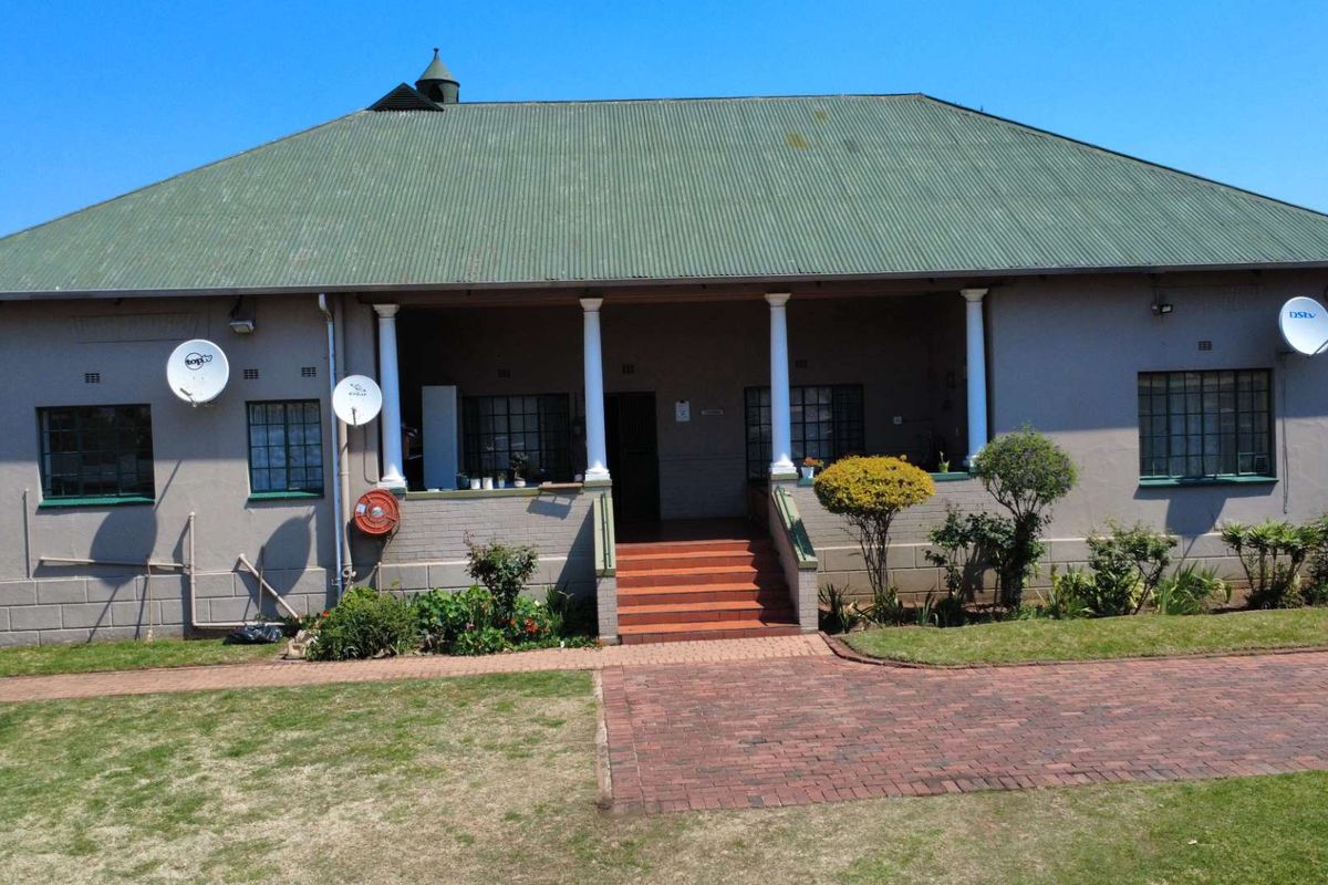 Front elevation of a single-story house featuring a covered veranda, brick steps, and a corrugated metal roof with a paved driveway.