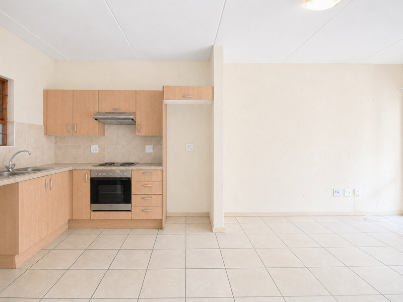 Open-plan kitchen and living area featuring light wood cabinetry, built-in oven, electric hob, and neutral tiled flooring throughout.