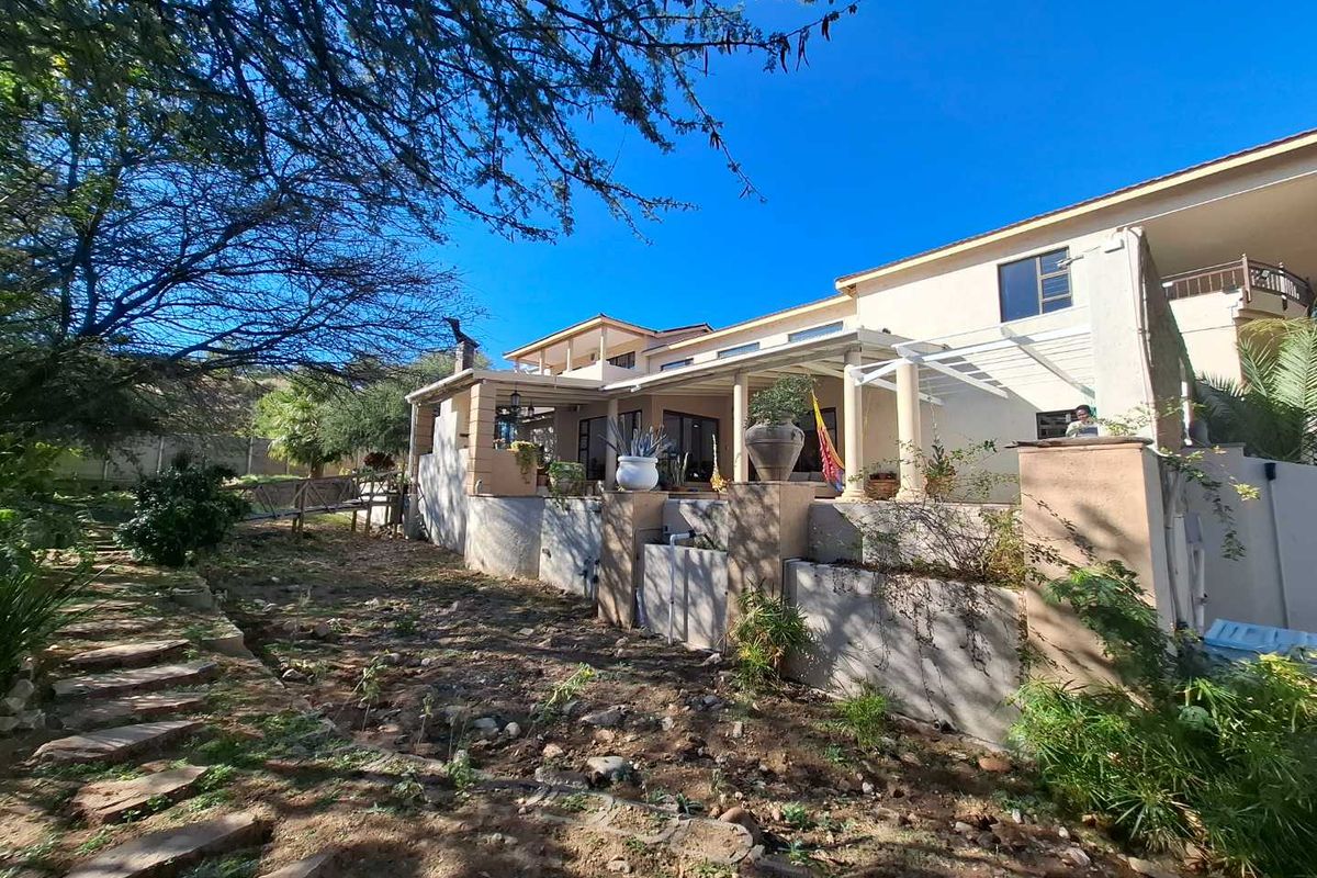 Rear view of the house featuring a covered patio area, stone pathway, and tiered garden landscaping.
