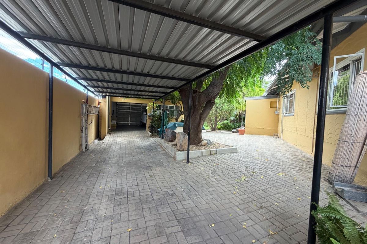 A paved driveway area featuring a covered carport structure, mature tree, and access to a garage, providing functional off-street parking.