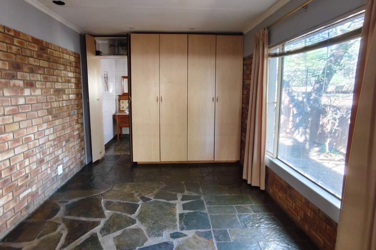 A bedroom featuring a large built-in wardrobe, exposed brick feature wall, and natural stone flooring with a view of the garden.