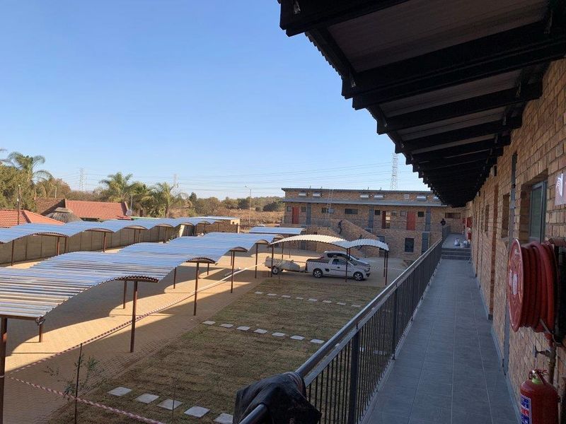 An elevated view of the apartment complex exterior, featuring a covered walkway, brick facade, and a paved parking area with multiple carports.