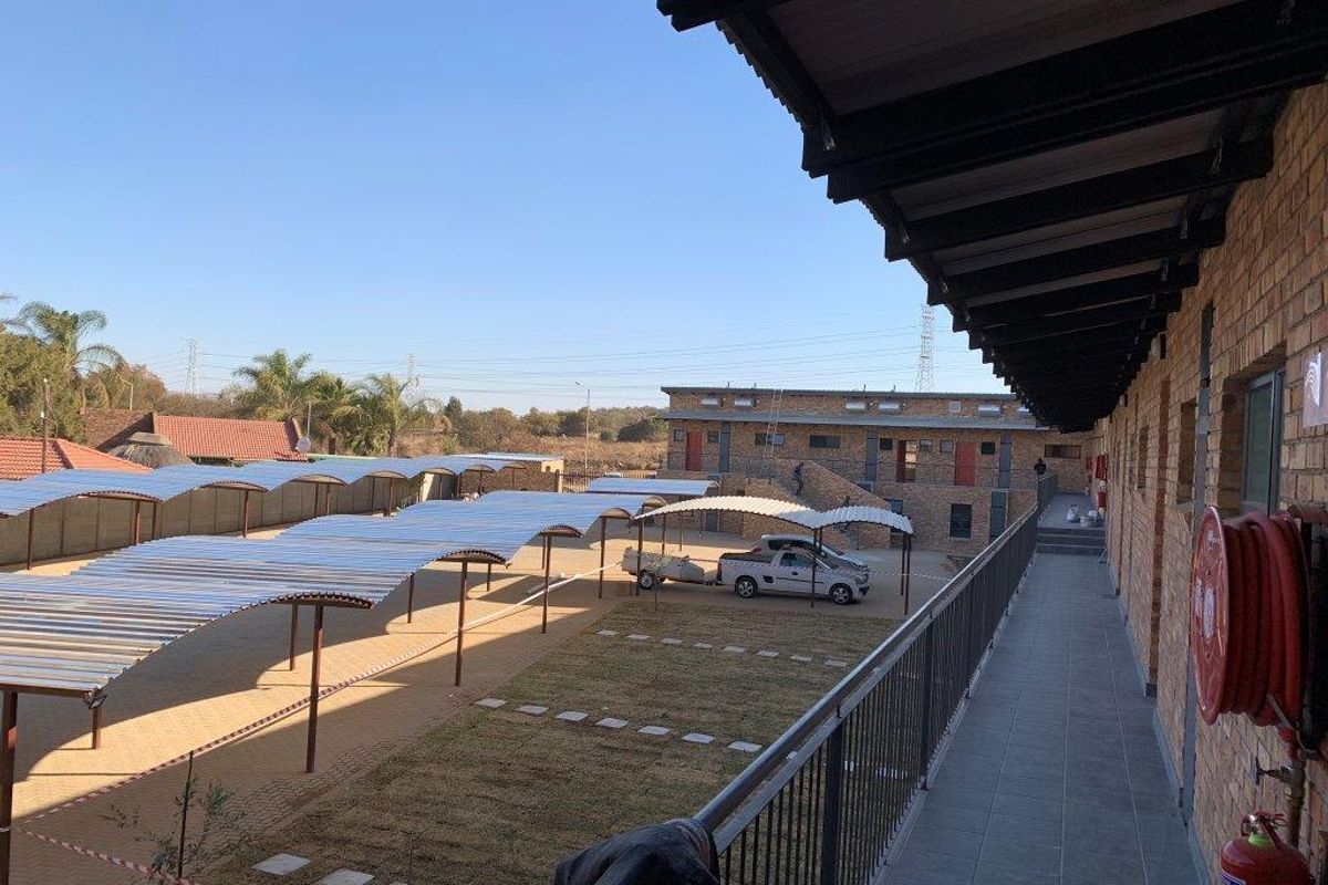 An elevated view of the apartment complex exterior, featuring a covered walkway, brick facade, and a paved parking area with multiple carports.