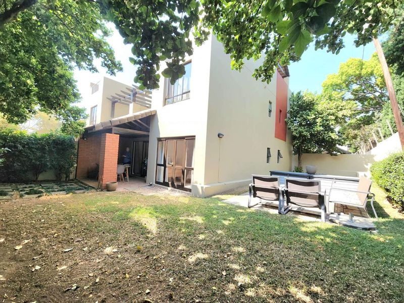 Rear view of the apartment featuring a covered patio with a timber pergola, brick detailing, and a private garden area.
