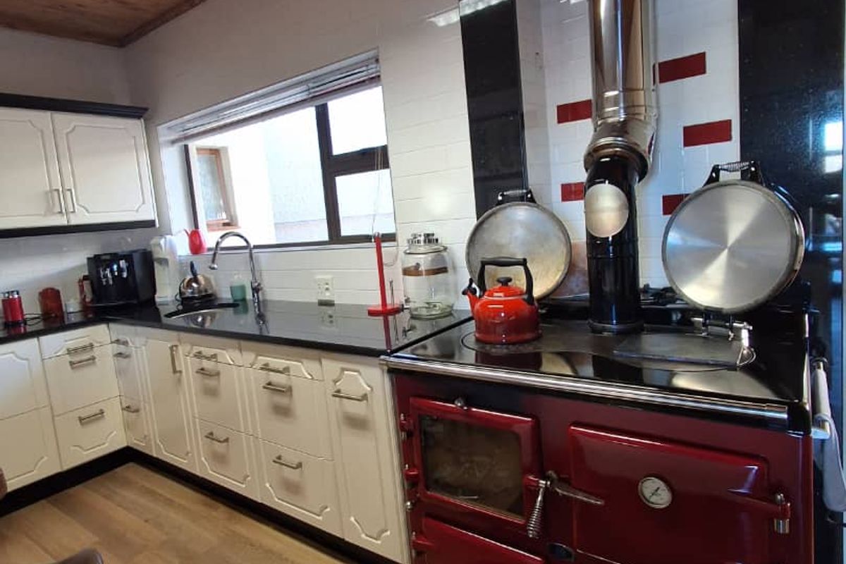 A kitchen featuring a prominent red range cooker, black granite countertops, white cabinetry, and a timber-paneled ceiling.