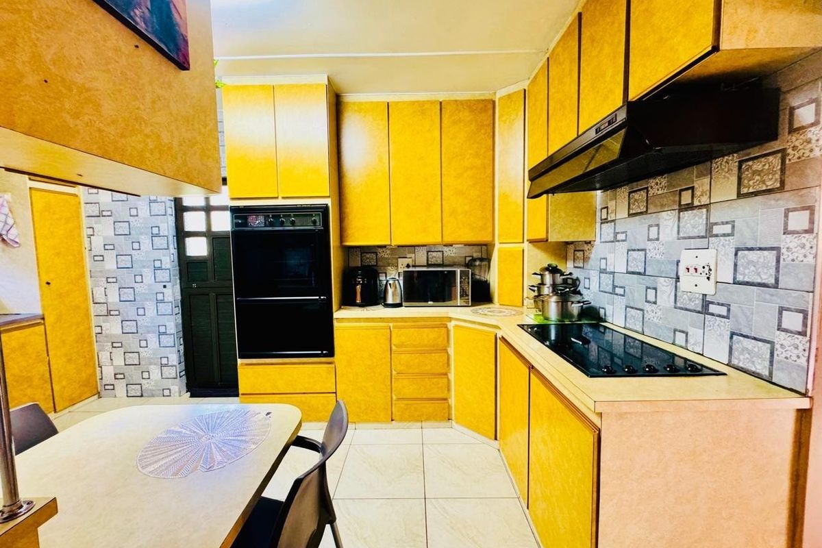 A functional kitchen featuring yellow cabinetry, a built-in oven, electric hob with extractor fan, and patterned tiled backsplash.