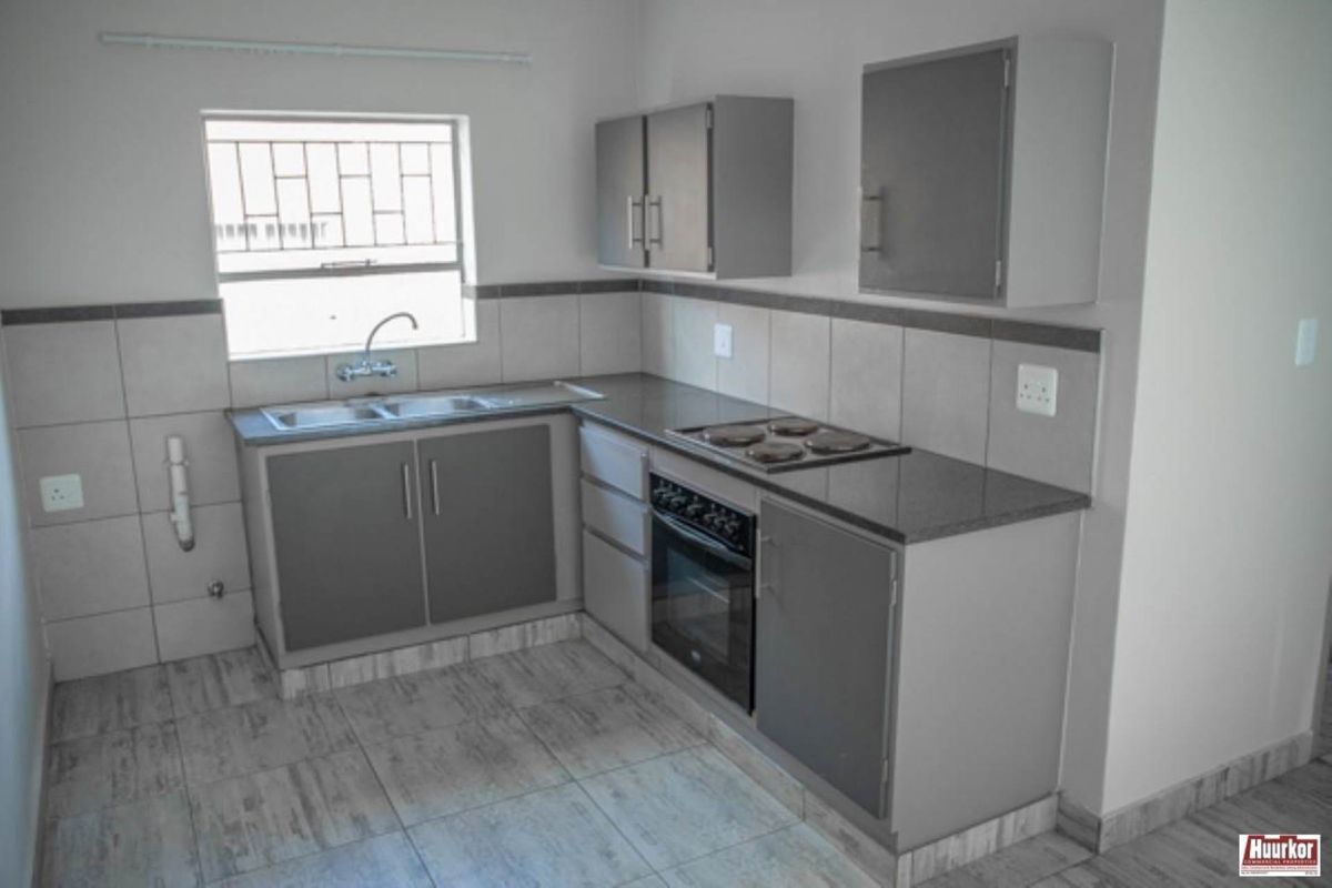 A clean, functional kitchen featuring grey built-in cabinetry, granite countertops, a built-in oven and hob, and tiled finishes throughout.