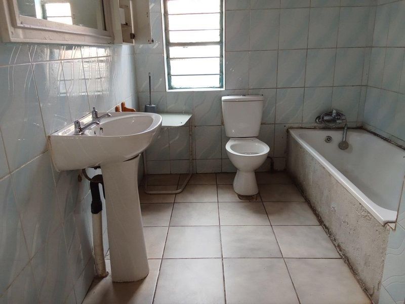 A functional bathroom featuring a pedestal basin, toilet, and bathtub with tiled finishes, requiring cosmetic updates to modernize the space.