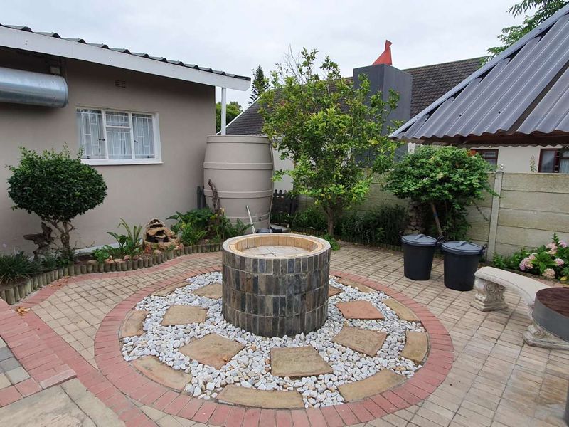 Outdoor paved patio area featuring a central stone-clad fire pit, covered seating structure, and integrated water storage tank.