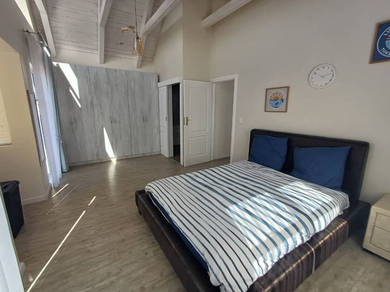 Spacious bedroom featuring high vaulted ceilings with exposed beams, built-in cabinetry, and light wood-look flooring.