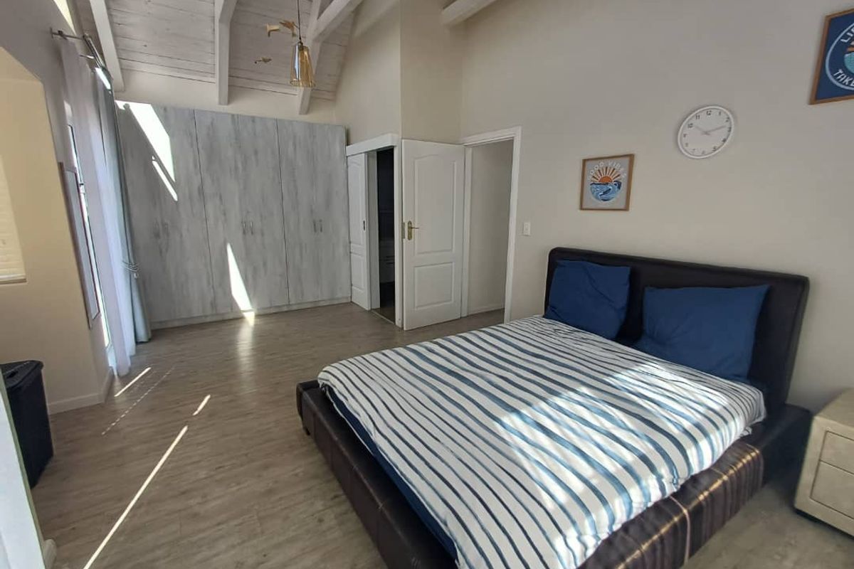 Spacious bedroom featuring high vaulted ceilings with exposed beams, built-in cabinetry, and light wood-look flooring.