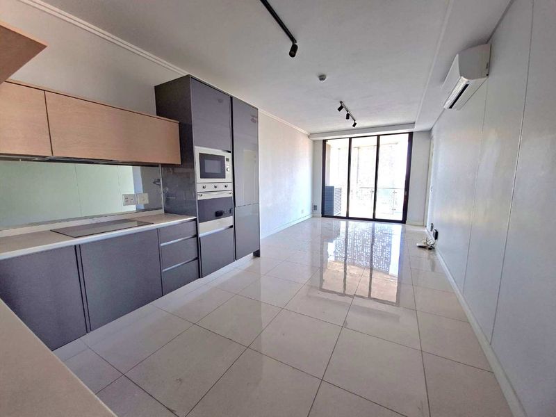 Modern open-plan living area featuring a sleek kitchen with integrated appliances, tiled flooring, and large sliding doors leading to an outdoor space.