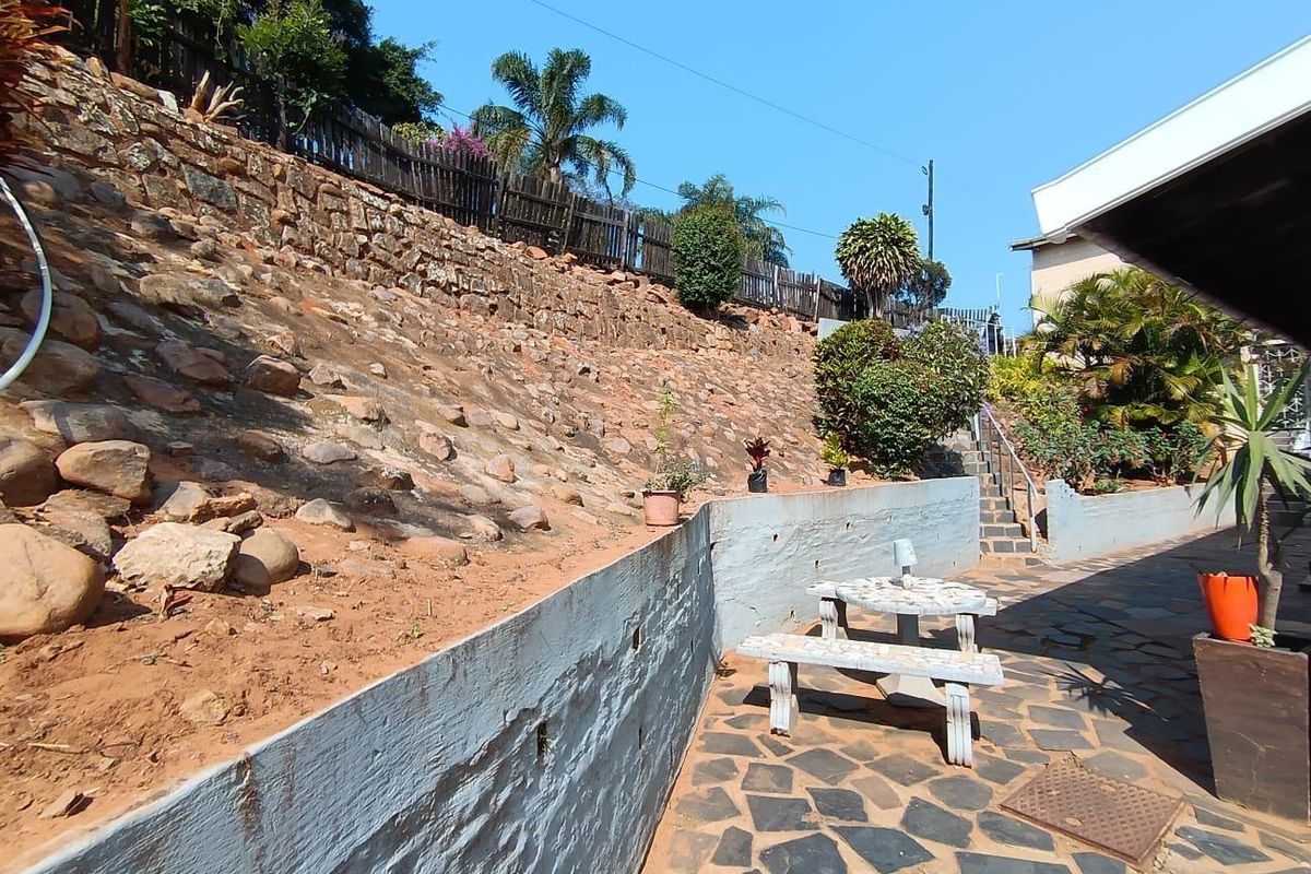 Rear outdoor area featuring a stone retaining wall, flagstone paving, and a concrete staircase leading to the upper garden level.