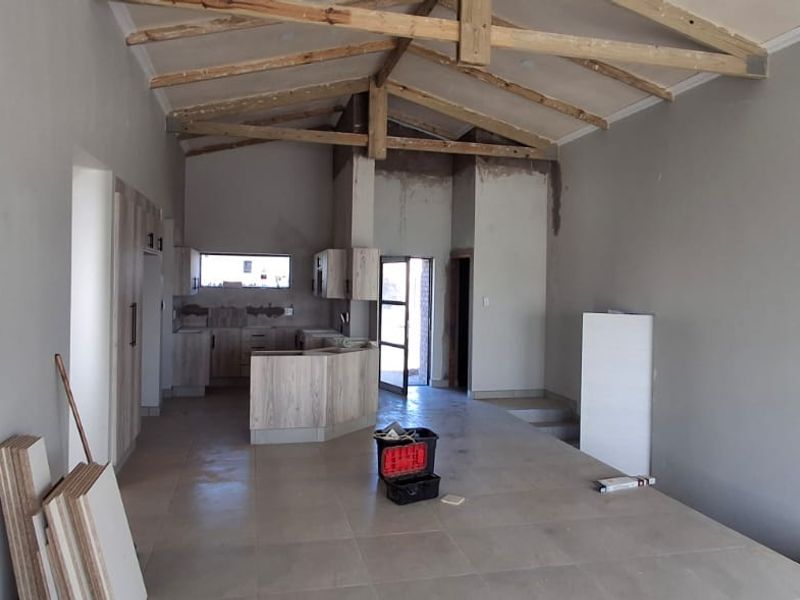 An open-plan living and kitchen area featuring vaulted ceilings with exposed timber trusses, tiled flooring, and partially installed kitchen cabinetry in a construction phase.