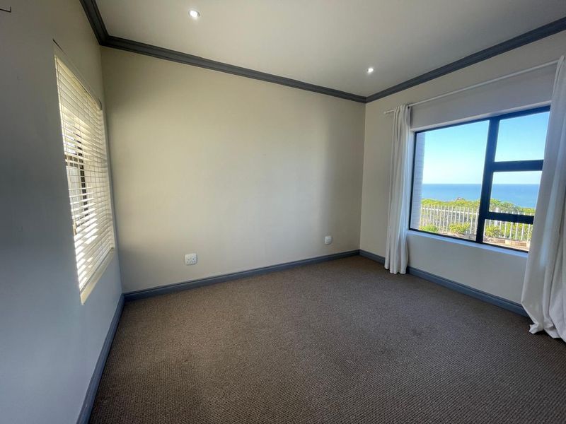 A bright, empty bedroom featuring neutral walls, carpeted flooring, and large windows offering a scenic ocean view.