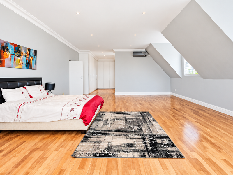 Spacious bedroom featuring polished hardwood flooring, built-in cabinetry, recessed lighting, and an air conditioning unit under a distinctive sloped ceiling.