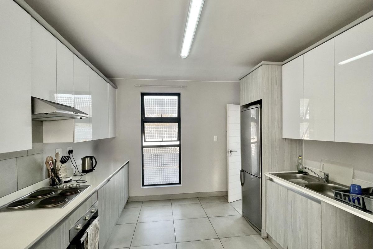 Modern galley-style kitchen featuring white high-gloss cabinetry, integrated electric hob, oven, extractor fan, and double sink with tiled flooring.