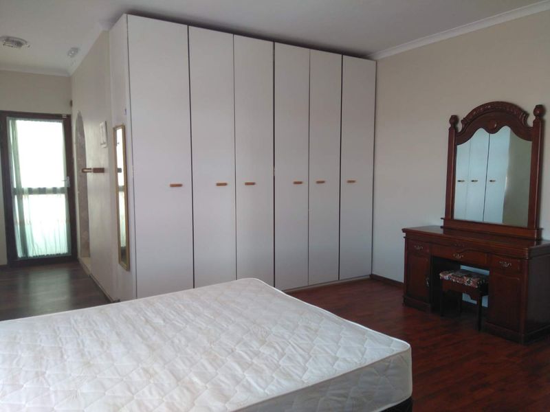 A bedroom featuring laminate flooring, a large white built-in wardrobe, and a glass panel door leading to an adjacent space.