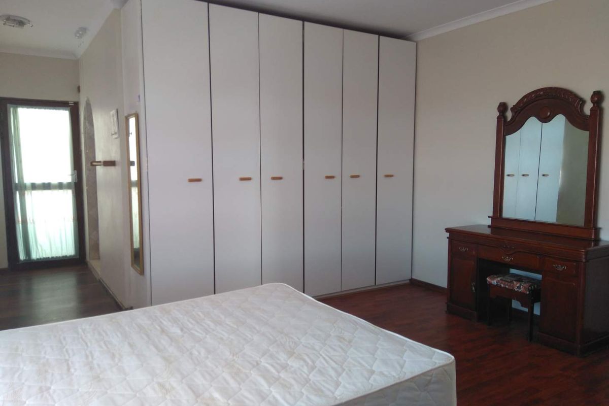 A bedroom featuring laminate flooring, a large white built-in wardrobe, and a glass panel door leading to an adjacent space.