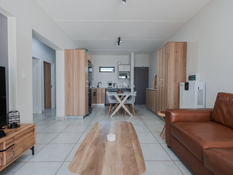A modern open-plan living and kitchen area featuring light wood-look cabinetry, neutral tiled flooring, and a functional layout connecting the kitchen to the living space.