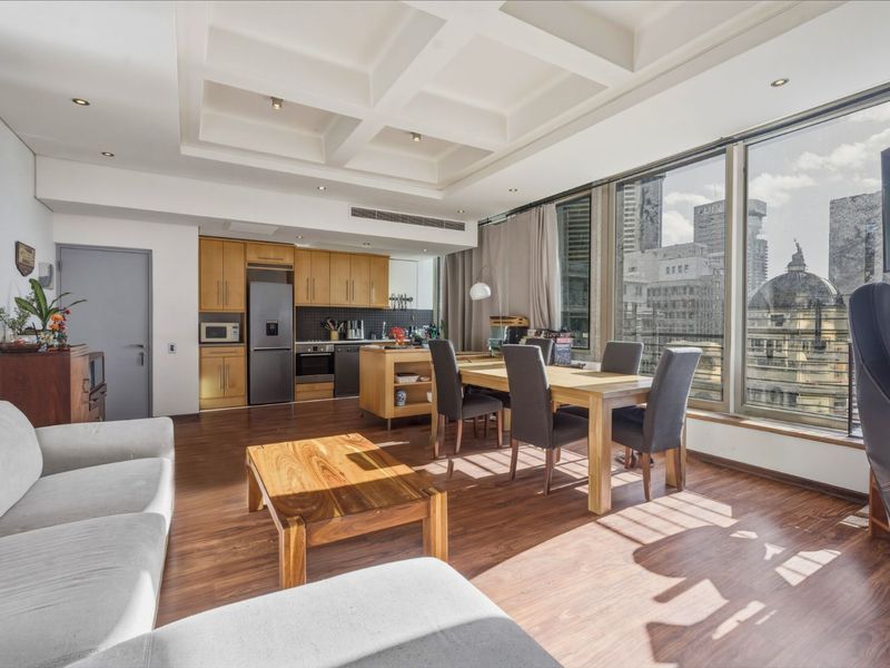 Spacious open-plan living and dining area featuring a modern kitchen, coffered ceilings, and expansive windows offering panoramic city views.