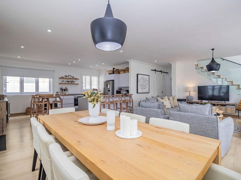 Spacious open-plan living area featuring a modern kitchen, dining space, and lounge, complemented by light wood flooring and a contemporary glass-railed staircase.
