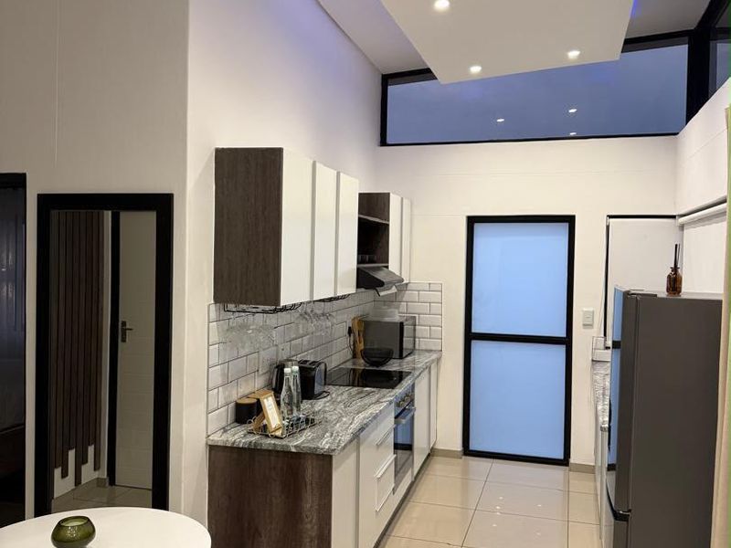 Modern kitchen featuring sleek two-tone cabinetry, stone countertops, subway tile backsplash, integrated appliances, and high ceilings with recessed lighting.