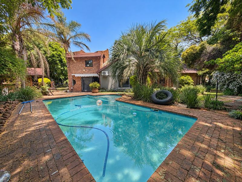 A well-maintained swimming pool area featuring brick paving and established garden surroundings, set against a classic brick residential facade.