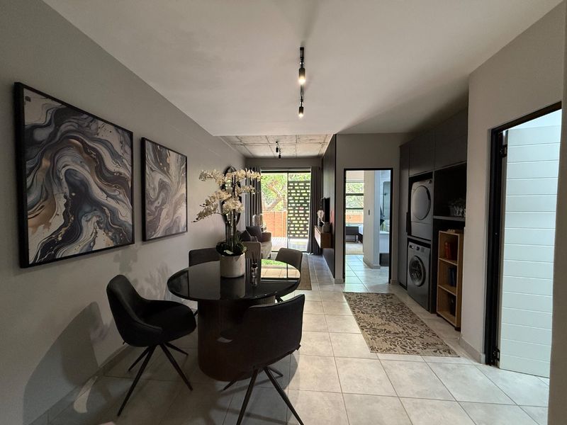 Modern open-plan living area featuring tiled floors, exposed concrete ceiling, track lighting, and integrated laundry cabinetry with a seamless flow to the outdoor space.
