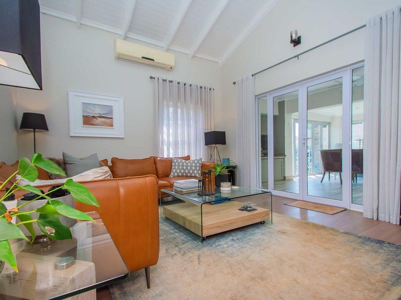 Bright living room featuring a high vaulted ceiling with exposed rafters, laminate flooring, and large sliding glass doors leading to an outdoor area.