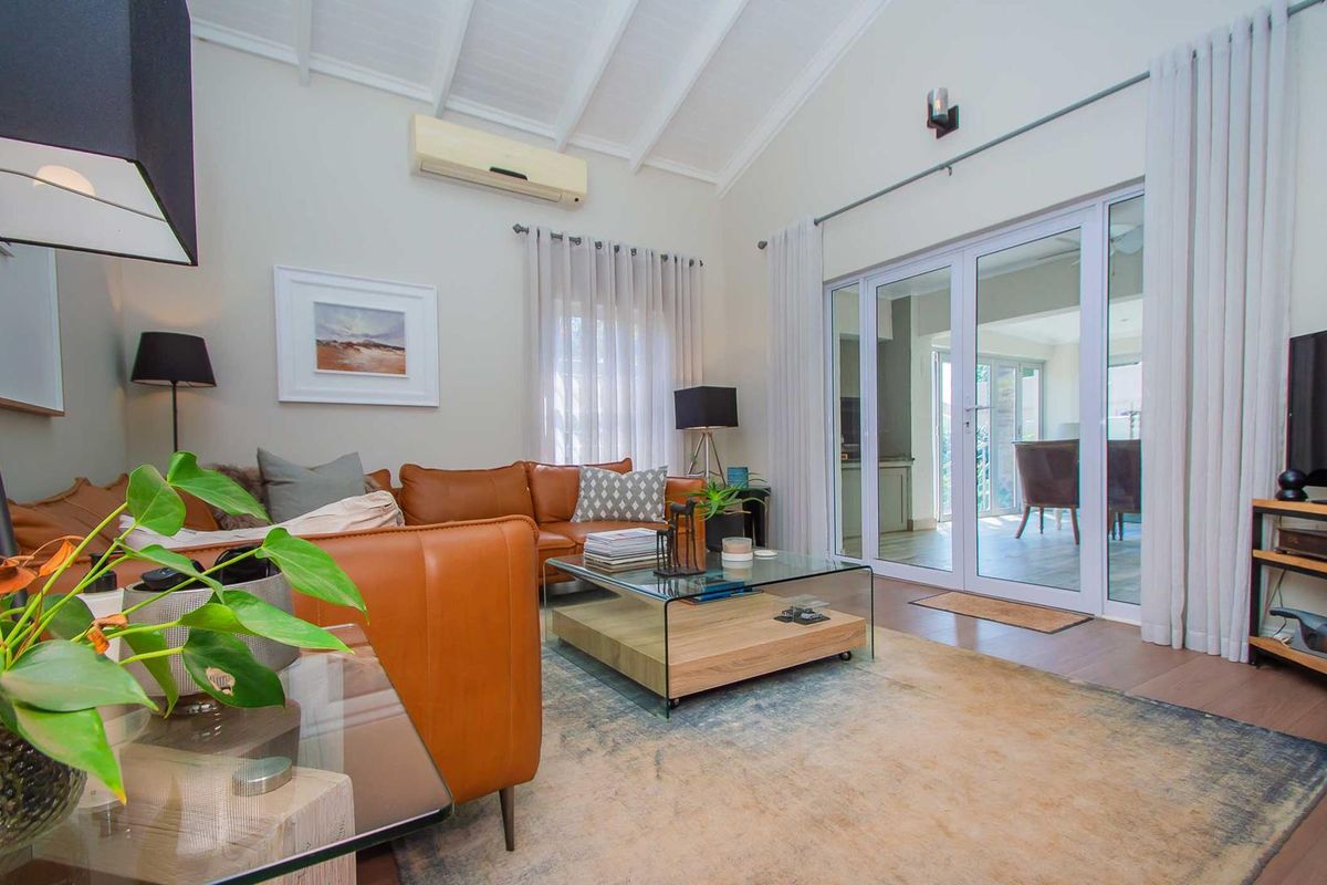 Bright living room featuring a high vaulted ceiling with exposed rafters, laminate flooring, and large sliding glass doors leading to an outdoor area.