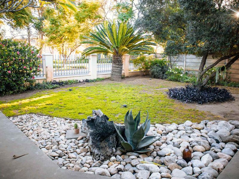A well-maintained garden area featuring a lawn, mature trees, stone landscaping, and secure perimeter fencing.