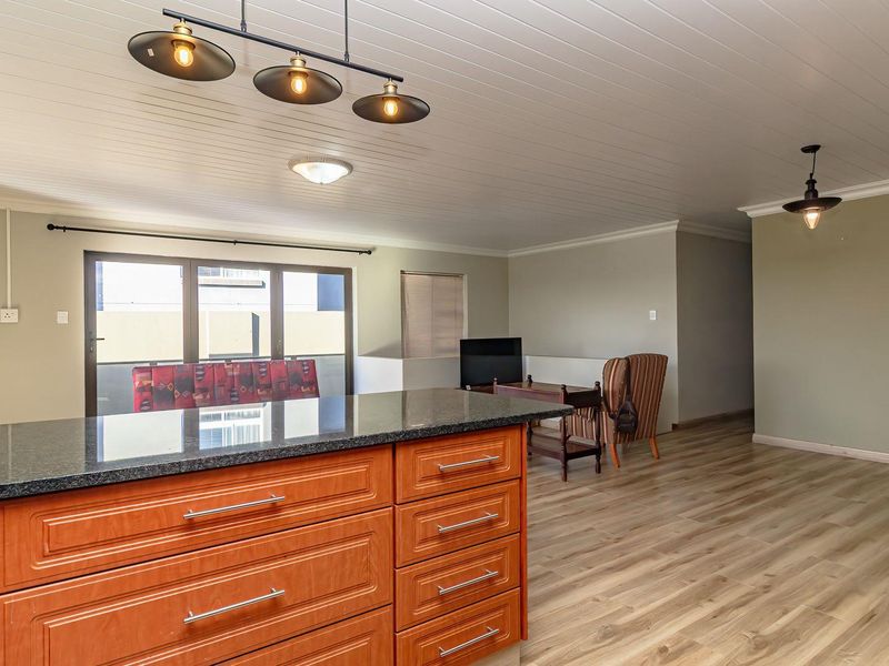 Spacious open-plan living area featuring a kitchen island with granite countertops, timber cabinetry, laminate flooring, and modern pendant lighting.