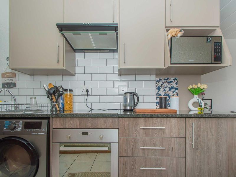 Modern kitchen featuring subway tile backsplash, granite countertops, built-in oven, extractor fan, and integrated cabinetry with a built-in microwave and washing machine.