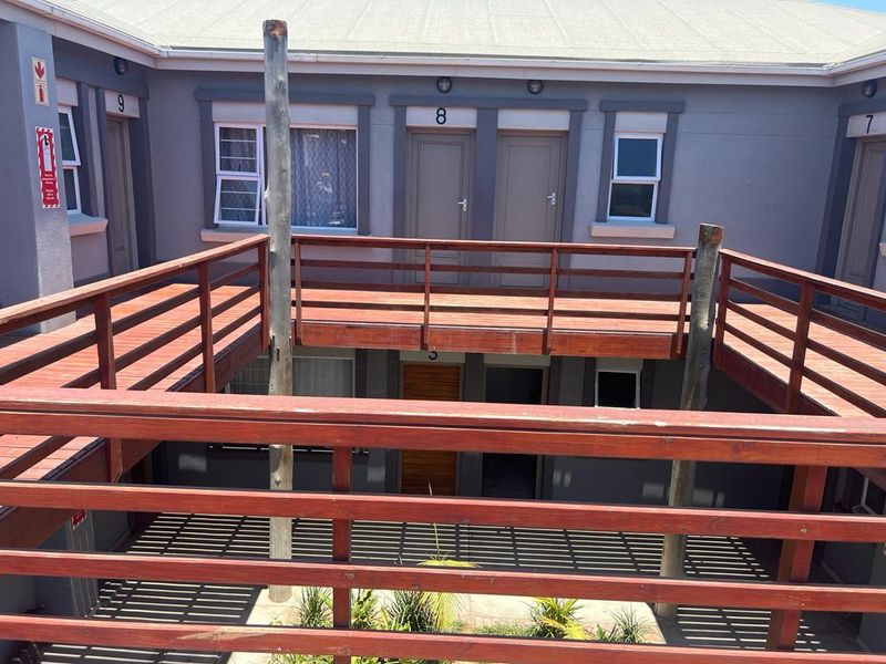 Exterior view of an apartment complex featuring a wooden balcony walkway with timber support posts and multiple unit entrances.