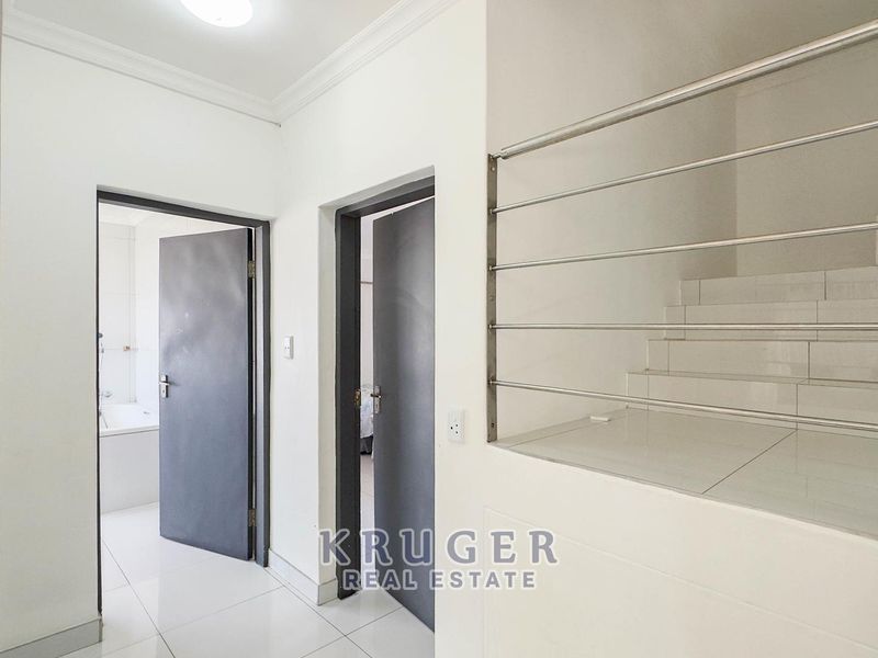 A clean, modern hallway featuring tiled flooring, internal doors, and a staircase with a stainless steel balustrade.