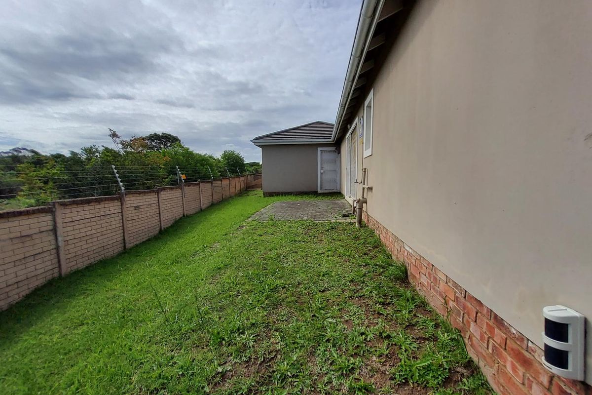 A rear exterior view of the townhouse featuring a paved patio area, perimeter brick wall with electric fencing, and a grassed garden space.