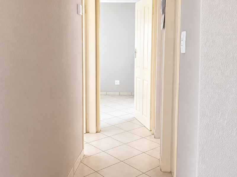 A clean, neutral-toned hallway featuring tiled flooring and access to multiple rooms through internal doors.