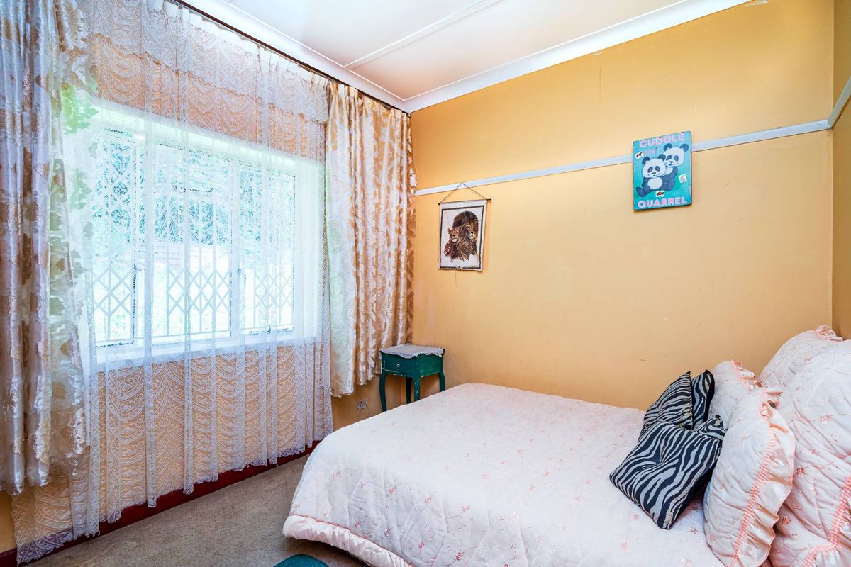 A bedroom featuring a window with security gate, coving, and a picture rail. The room requires cosmetic updates to modernize the space.
