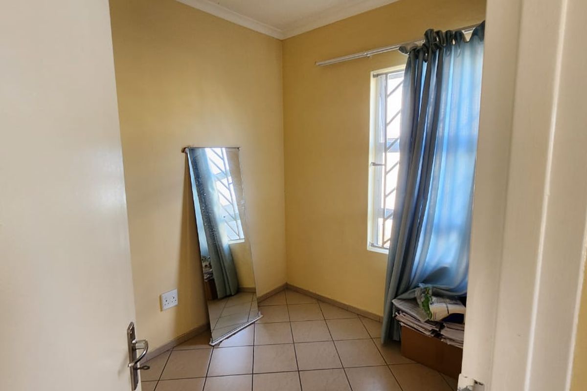 A compact bedroom featuring tiled flooring, a window with security bars, and neutral wall finishes, offering a clean and functional space.