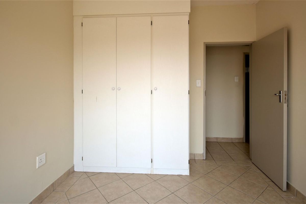 A bedroom featuring built-in white cabinetry, tiled flooring, and a neutral color palette, providing a clean and functional living space.