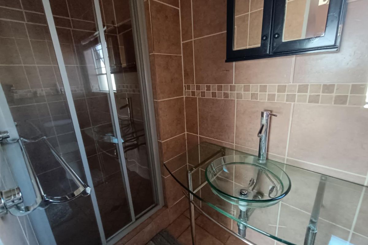 A compact bathroom featuring a glass vessel sink with a chrome mixer, glass vanity, and a tiled shower enclosure.